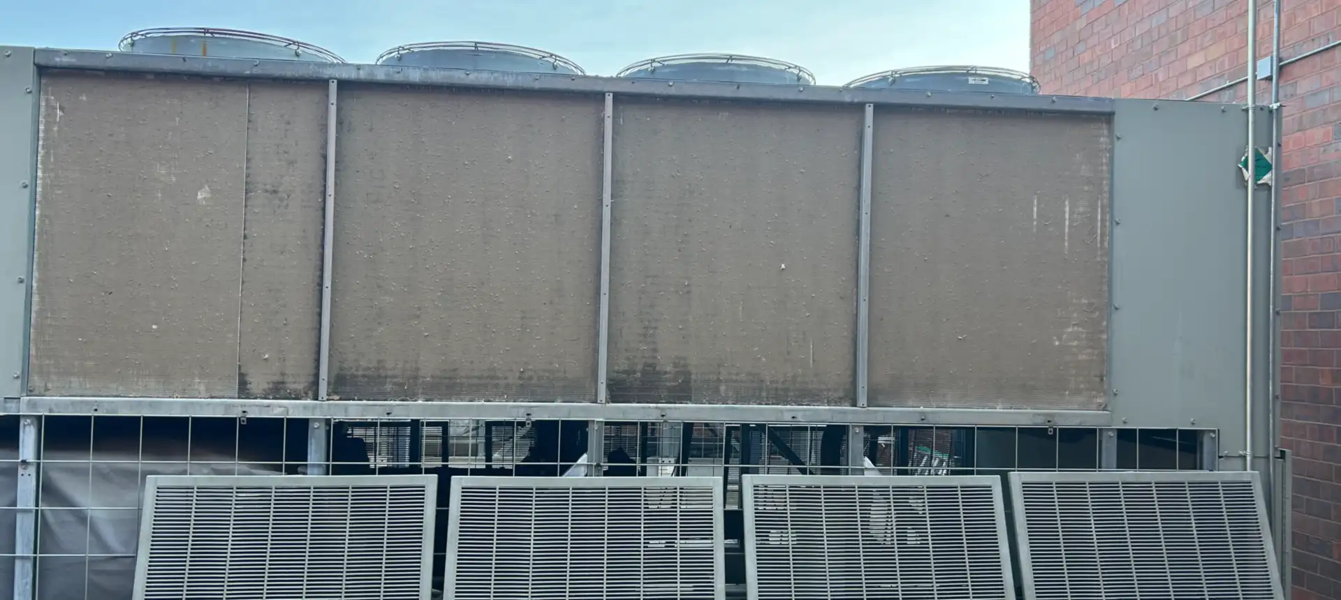 Commercial cooling tower with four top-mounted fans and weather-stained intake faces, its louvred panels set out on the ground in front of it