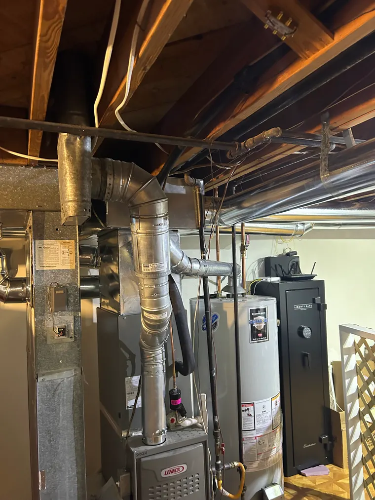 Lennox gas furnace in a basement, its new sheet-metal plenum and flue routed up between the floor joists, with two gas water heaters alongside