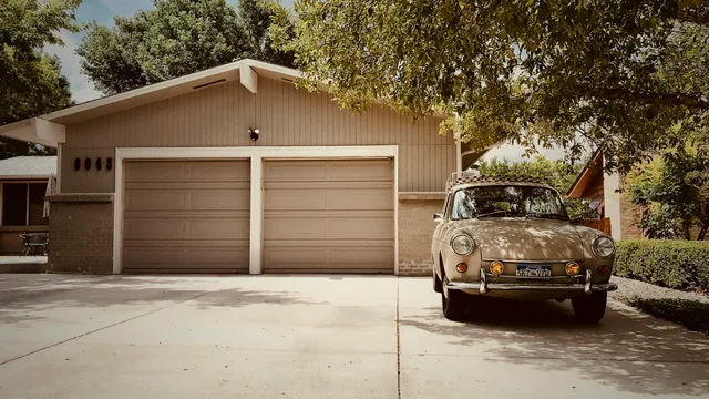 A two-car attached garage on a single-storey ranch house, its pale sectional doors facing a concrete driveway under mature shade trees