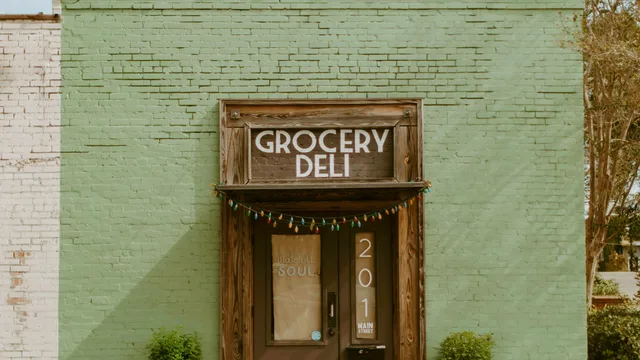 The painted brick storefront of a small-town grocery and deli, its hand-lettered sign above the door — the kind of independent food business that runs a single walk-in cooler