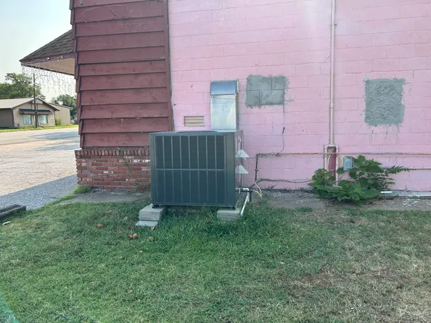 Packaged heating and cooling unit set on concrete blocks against a painted block wall, its galvanized duct and gas line run in at the wall