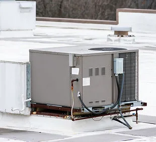 Packaged rooftop unit standing on a white membrane roof, with its electrical disconnect and refrigerant lines run down one side
